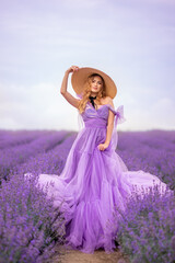 beautiful woman in a lush lilac dress in a field of lavender. She's wearing a big braided hat