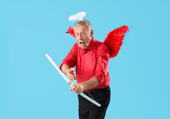 Shocked mature man dressed as Cupid with bow on blue background. Valentine's Day celebration