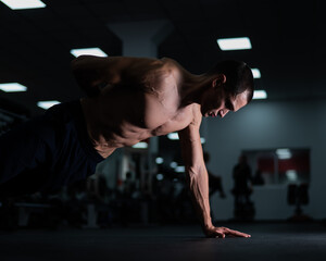 Fototapeta na wymiar Muscular shirtless man doing one-arm push-ups in the gym. 