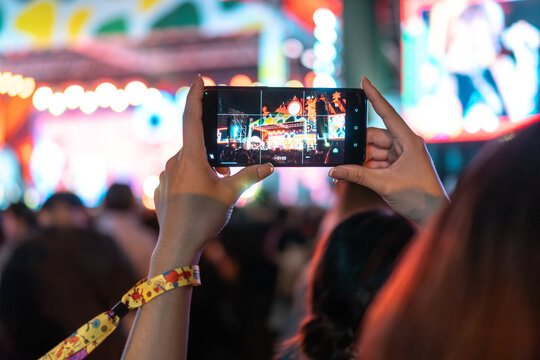 Girl holding smart phone and recording and photographing in music festival concert, event background concept	
