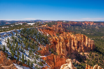Panorama over Bryce Canyon from a high viewpoint, snow remaining on the ground, clear blue sky,...