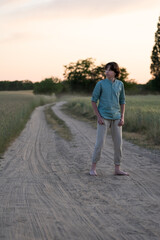 Obraz premium A barefoot teenager in comfortable clothes stands on a dirt road.