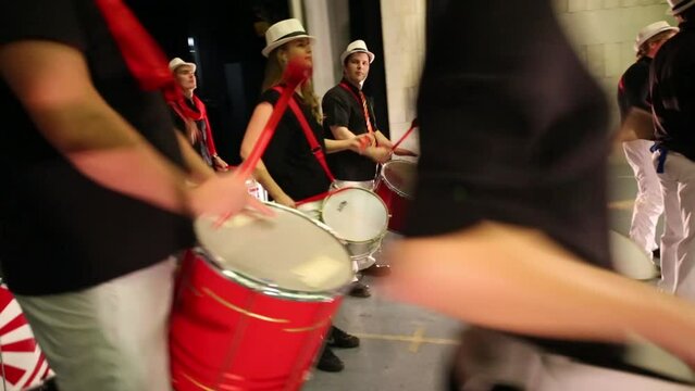 Musical group of fourteen people in hats play drums 