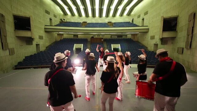 Musical group of fourteen people in hats with drums wave sticks 