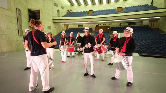 Musical group of fourteen people in hats with leader play drums