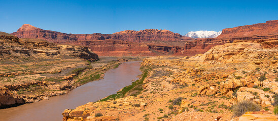 Fototapeta na wymiar Colorado river in southern Utah, USA, with snow capped mountains in the background. Arid terrain, desertic area, deep blue sky.
