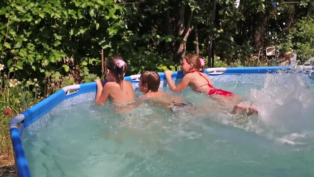 Happy boy and two girls splash by legs in swimming pool in garden