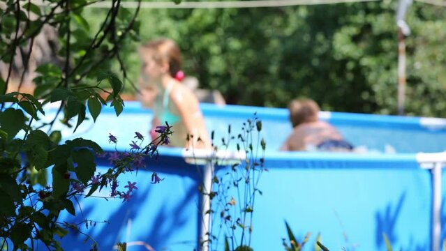 Three happy children play in swimming pool in summer garden