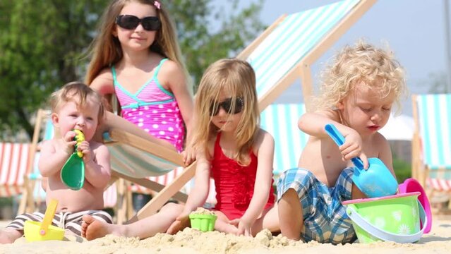Four children sit and play in sand by shovels, buckets.