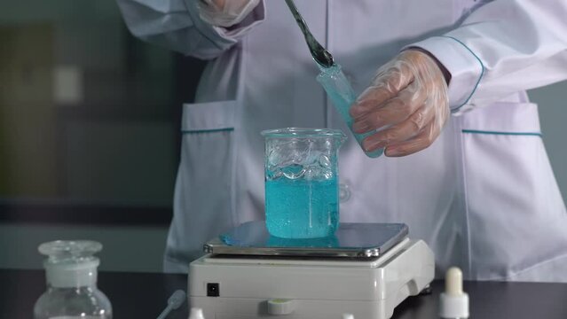 A scientist with a white coat in a laboratory collects a colored gel into a test tube