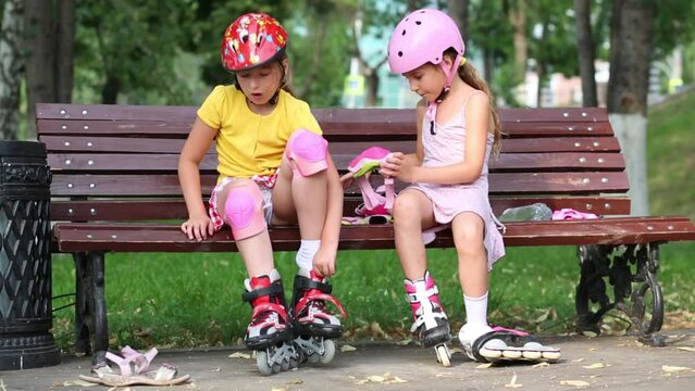 Two girls sit and put on rollers and protective knee