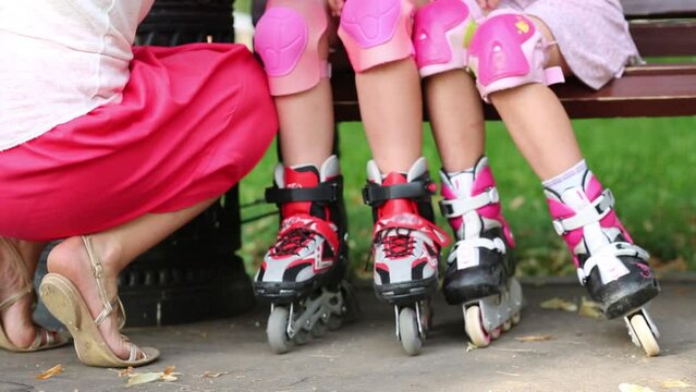 Two girls with rollers sit on bench and woman sits near them