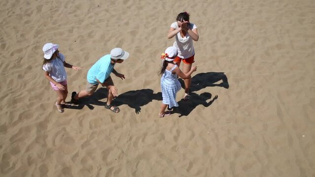 Woman with three happy children play blindman buff on sand