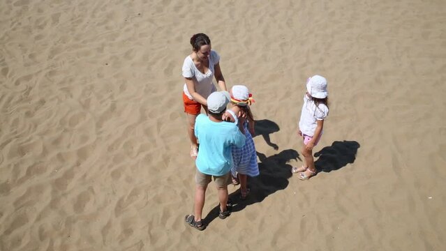 Woman with three children play blindman buff on yellow sand