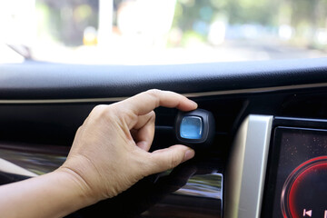 The driver's hand installs a blue car air freshener on the car AC air vent grille on the dashboard.