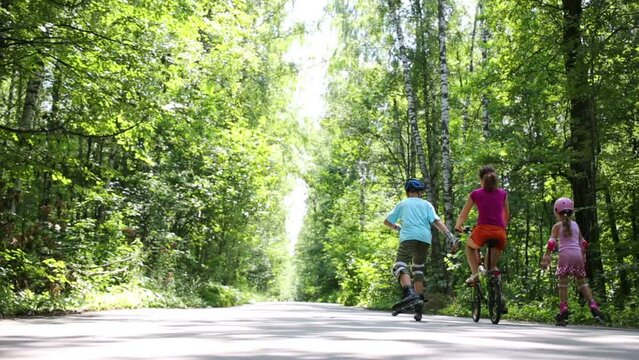 Back of boy and girl roller-skating and mother riding bicycle