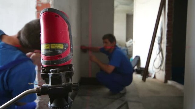 Two workers make measurements with laser level tool