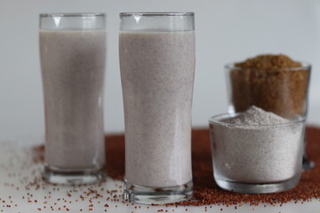 Ragi Malt. Two tall glasses of nutritious ragi porridge along with the ingredients ragi flour and raw sugar