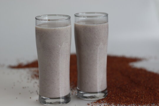 Ragi Malt, wholesome ragi delight. Two tall glasses of nutritious ragi porridge and a scattered spread of ragi grains around
