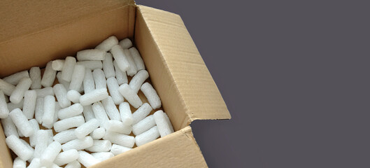 Opened cardboard packaging box with white polystyrene packing chips. Monochrome gray background. Copy space