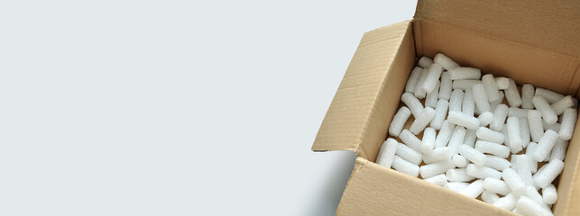 Opened cardboard packaging box with white polystyrene packing chips. Monochrome gray background. Copy space