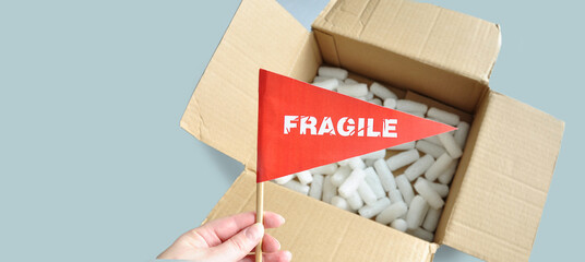 Opened cardboard packaging box with white polystyrene packaging chips. Tiny red paper flag in hand...