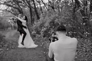 Fototapeta na wymiar Professional wedding photographer taking pictures of the bride and groom in nature in autumn