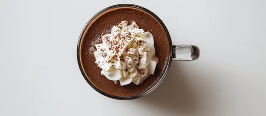  Top view of a white background with a glass cup of tasty hot chocolate topped with whipped cream. © AkuAku