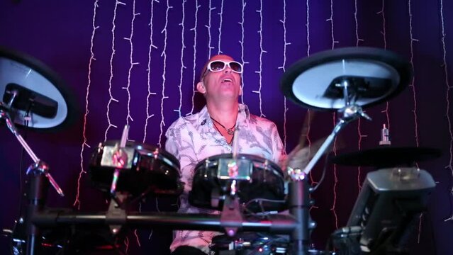 Bald middle aged man in sunglasses plays drum set in night club