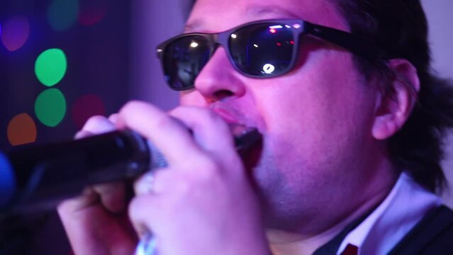 Young man in sunglasses plays harmonica to microphone at show