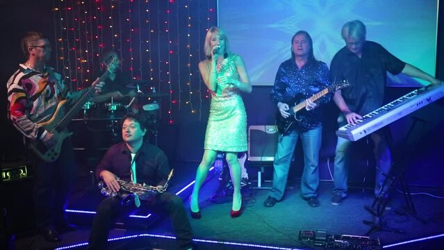 Musical band of five men and pretty woman performs on stage