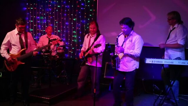 Group of five musicians with saxophone perform on show in club