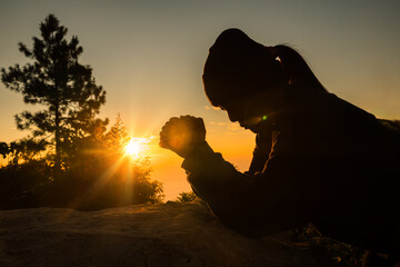 Silhouette of woman kneeling down praying for worship God at sky background. Christians pray to...