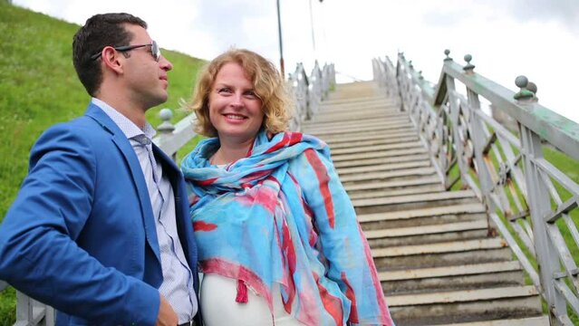 Pregnant woman and stylish man embrace on stairs, talk and smile