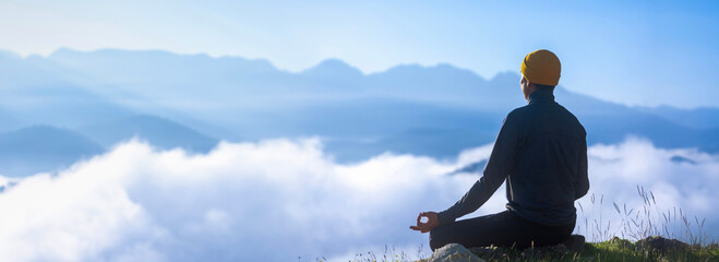Panorama back view of man is relaxingly practicing meditation yoga mudra at mountain top with mist and fog in summer to attain happiness from inner peace wisdom for healthy mind and soul concept