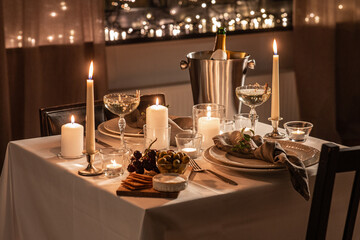 holidays, romantic date and celebration concept - close up of festive table serving for two with champagne bottle in ice bucket and candles burning at home on valentine's day - Powered by Adobe