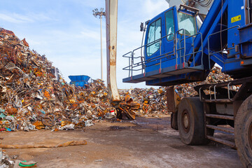 Dump of old rusty scrap metal with a crane with a boom with grabbing steel claws.