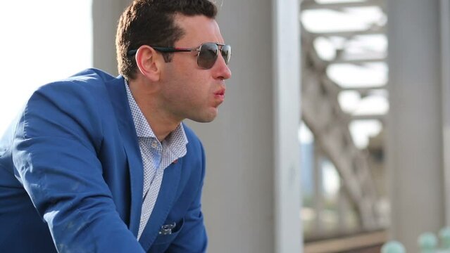 man in blue jacket and sunglasses smokes cigar on railway bridge
