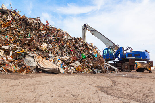 Dump of old rusty scrap metal with a crane with a boom with grabbing steel claws.