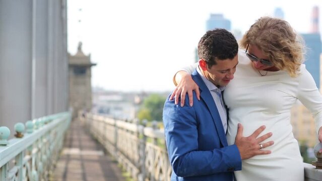 Pregnant woman and man embrace and kiss on railway bridge
