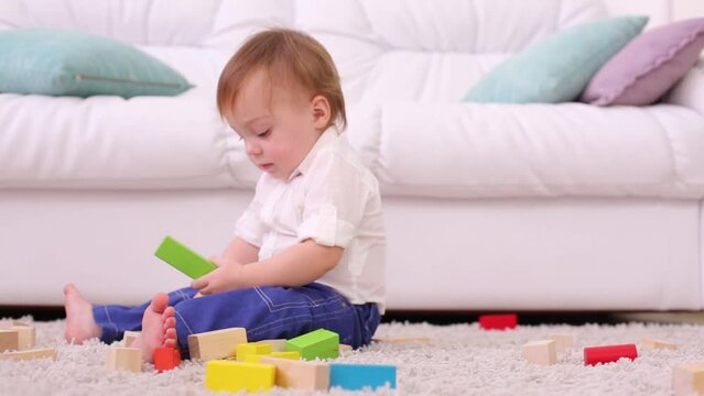Cute baby sits on soft carpet among tinker toys and shouts