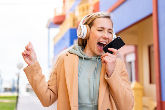 Young blonde woman at outdoors listening music with a mobile and singing