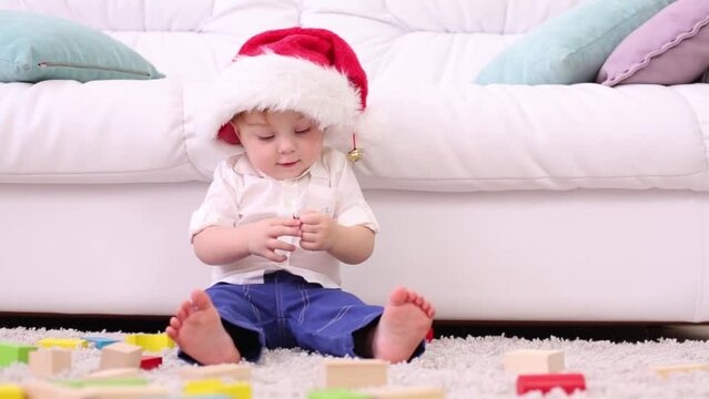 Cute little kid in red cap sits near couch among tinker toys