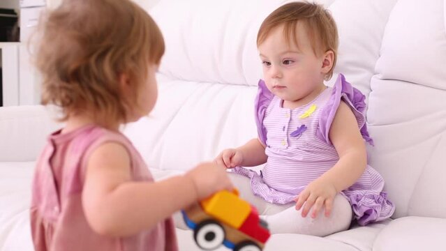 Little girl does not give other girl on white sofa toy car