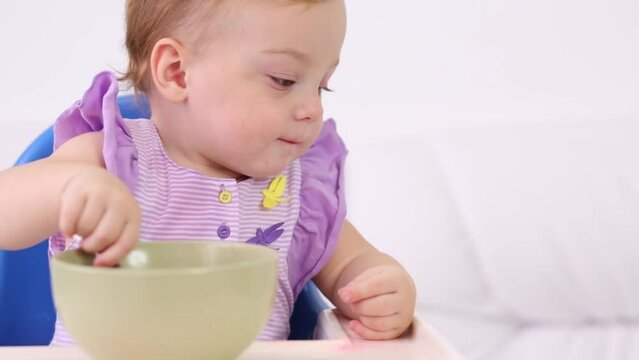 Little cute baby sits at highchair and eats porridge