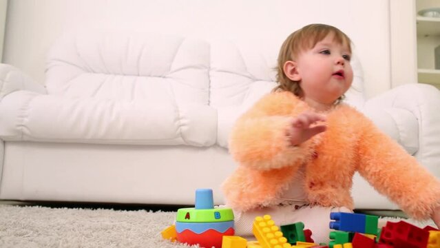 Cute little girl sits on carpet and plays with tinker toys