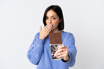 Young caucasian woman isolated on white background taking a chocolate tablet and surprised