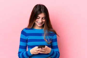 Young caucasian woman isolated on pink background sending a message with the mobile