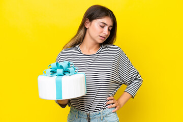 Young caucasian woman holding birthday cake isolated on yellow background suffering from backache for having made an effort