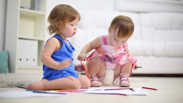 Two little kids draw by pencils on floor in room at home